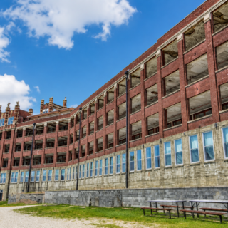 Abandoned historic red brick hospital building with dramatic cloudy sky during daytime