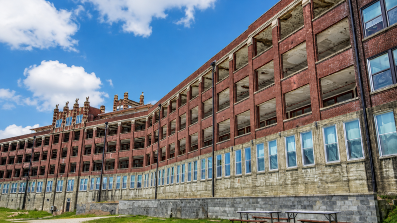 Abandoned historic red brick hospital building with dramatic cloudy sky during daytime